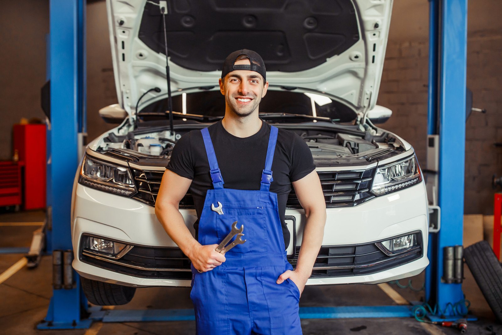 mechanic man in uniform holding wrenches in the auto service center and smiling at the camera